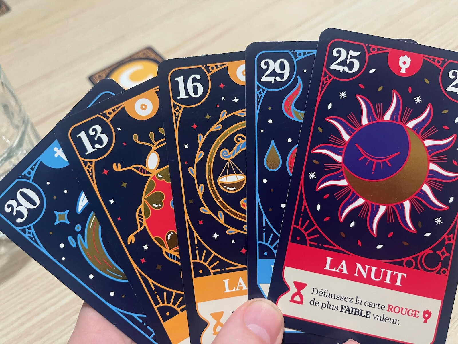Une main de cinq cartes de Présages, dont La Nuit et son effet : défausser la carte rouge de plus faible valeur