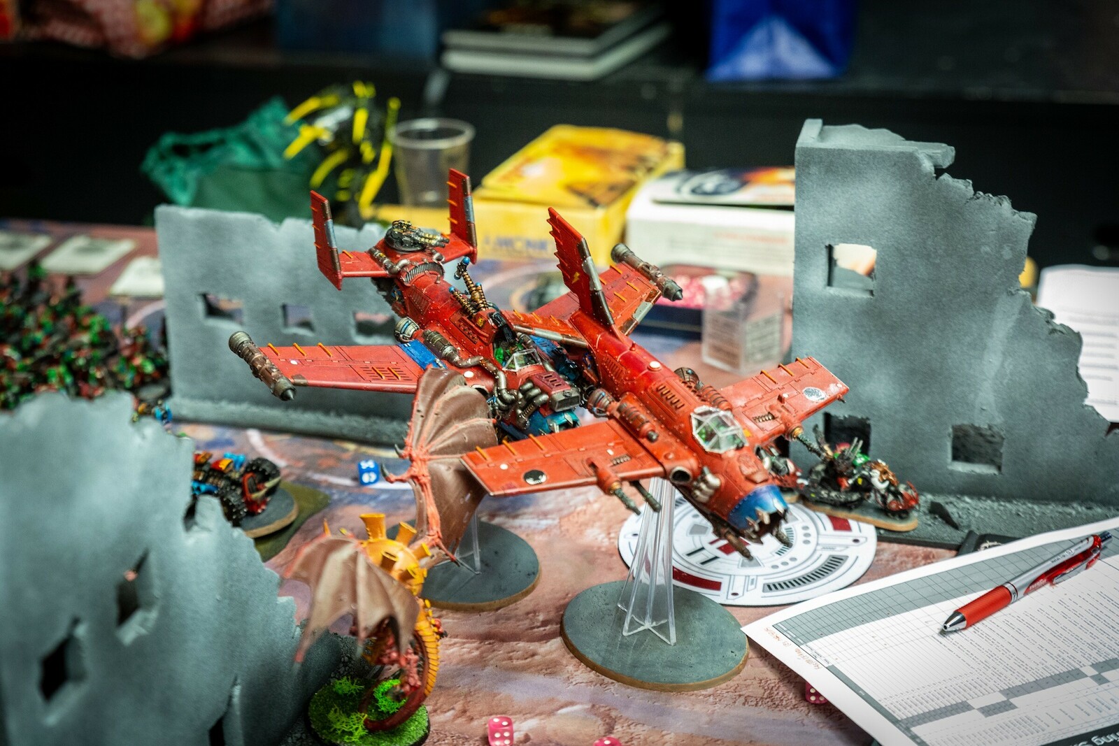 Des joueurs disputent des parties de Warhammer 40,000 sur des tables décorées, dans une grande salle de convention